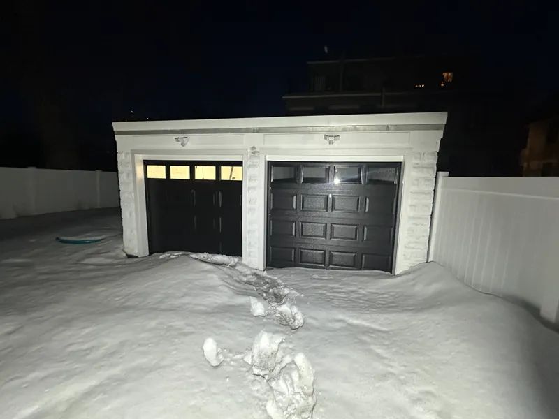 Black dual garage doors with windows on detached garage at night in deep snow